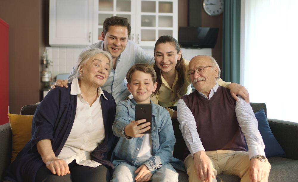 Familie sitzt gemeinsam auf dem Sofa und schaut auf Smartphone.
